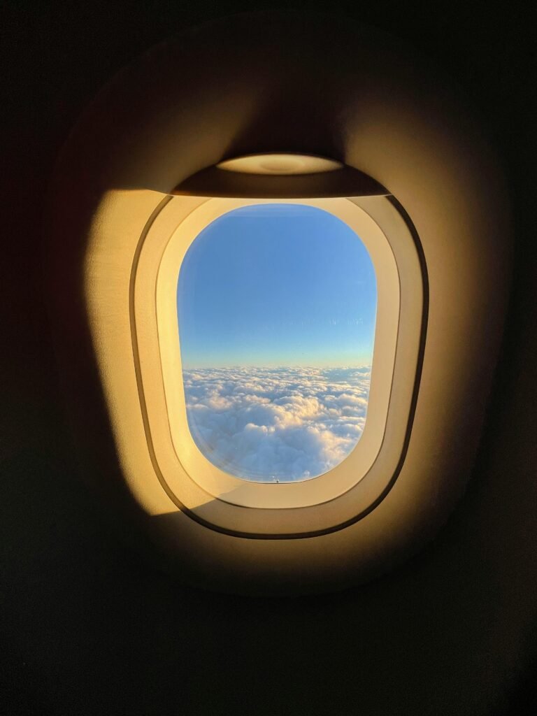 Bright clouds and blue sky seen through an airplane window at high altitude.